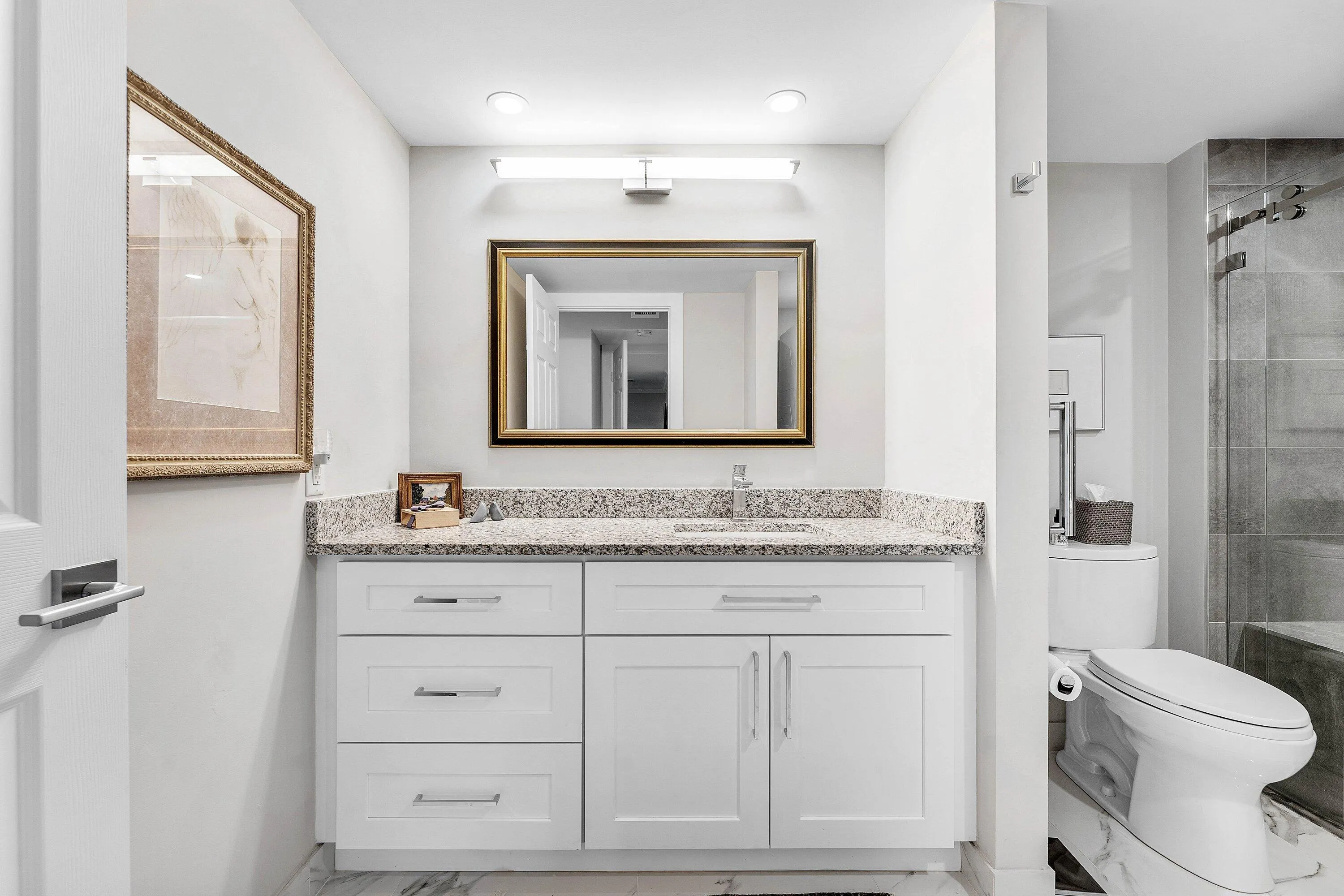 White shaker-style vanity with a light granite countertop, undermount sink, and polished chrome fixtures