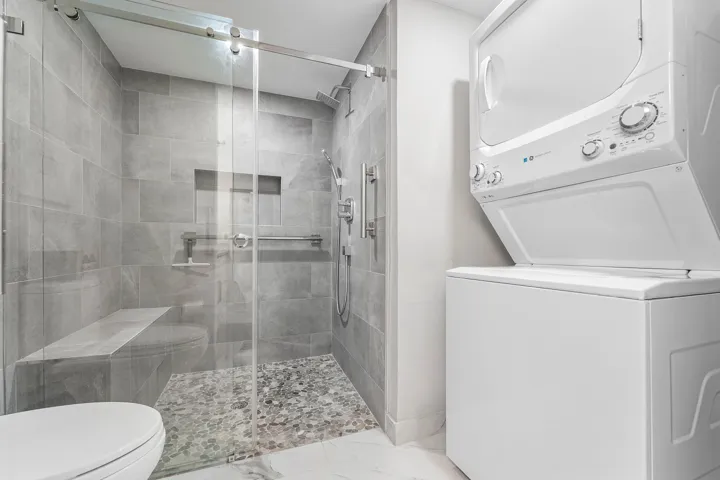 Glass-enclosed shower with a built-in bench, pebble-tiled floor, and a recessed niche