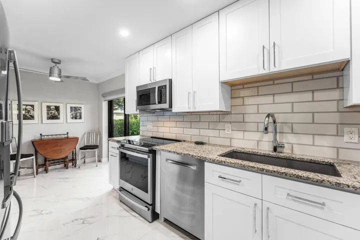 Kitchen featuring white cabinetry, stainless steel appliances, granite countertops, and a subway tile backsplash