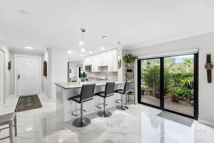 Gleaming white tile flooring, kitchen island with seating, pendant lighting, built-in cabinetry, and sliding glass doors to outdoor space