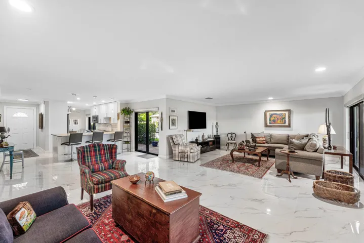 Spacious open-concept living area featuring polished tile flooring, recessed lighting, crown molding, and a sliding glass door