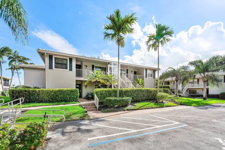 Two-story building with exterior access, featuring mature palm trees, manicured hedges, and brick pathways