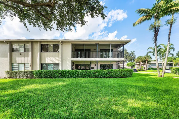 Exterior building featuring multiple screened balconies and patios, surrounded by mature landscaping and a well-maintained lawn