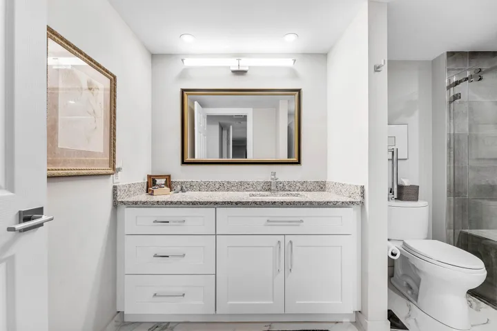 White shaker-style vanity with a light granite countertop, undermount sink, and polished chrome fixtures