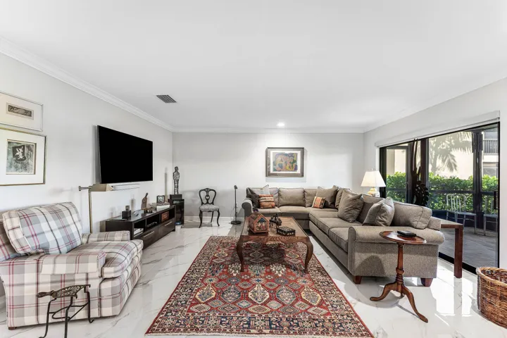 Spacious living area featuring white tile flooring, crown molding, and sliding glass doors