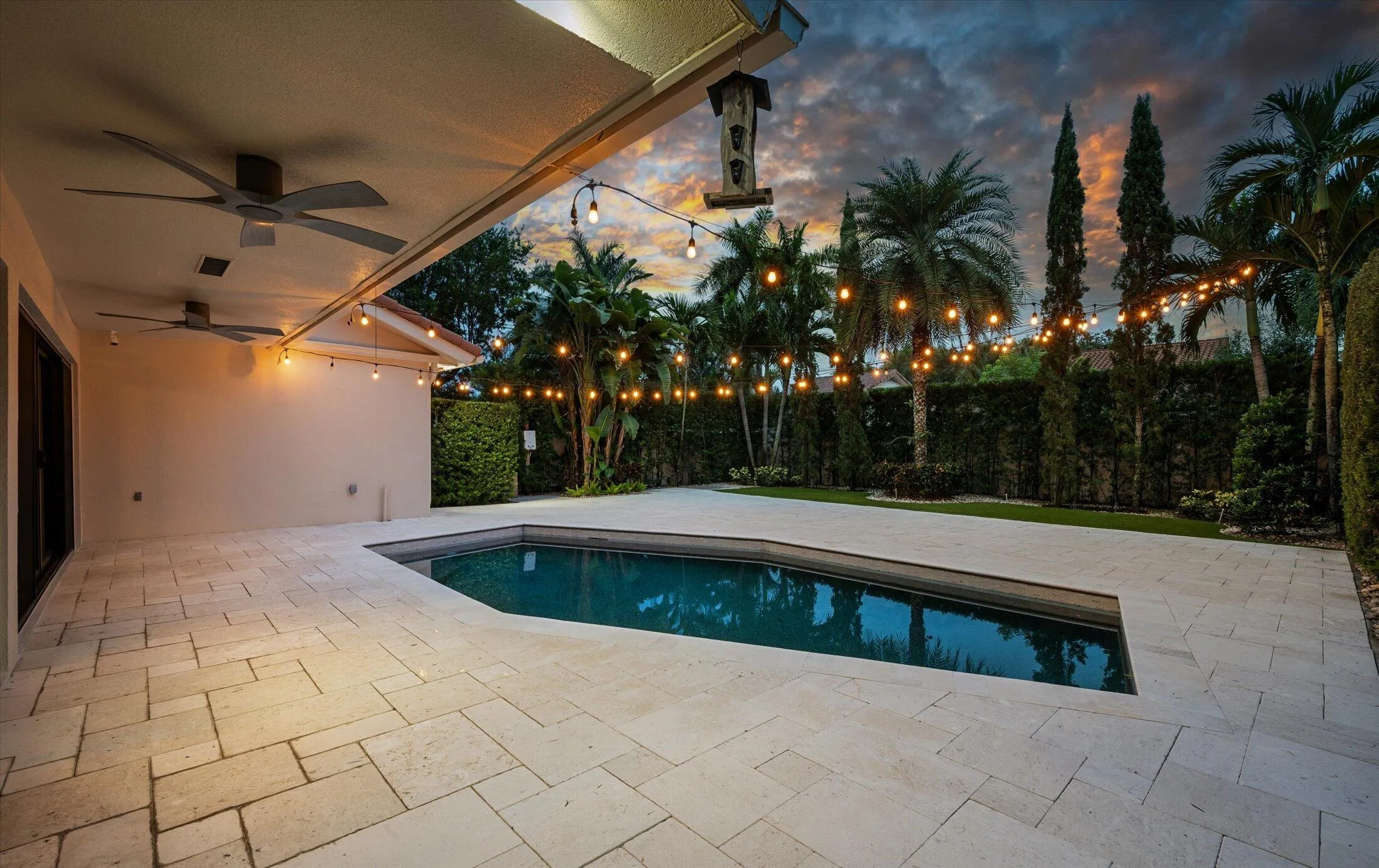 Expansive pool patio with light-toned paving stones, recessed lighting, and dual ceiling fans