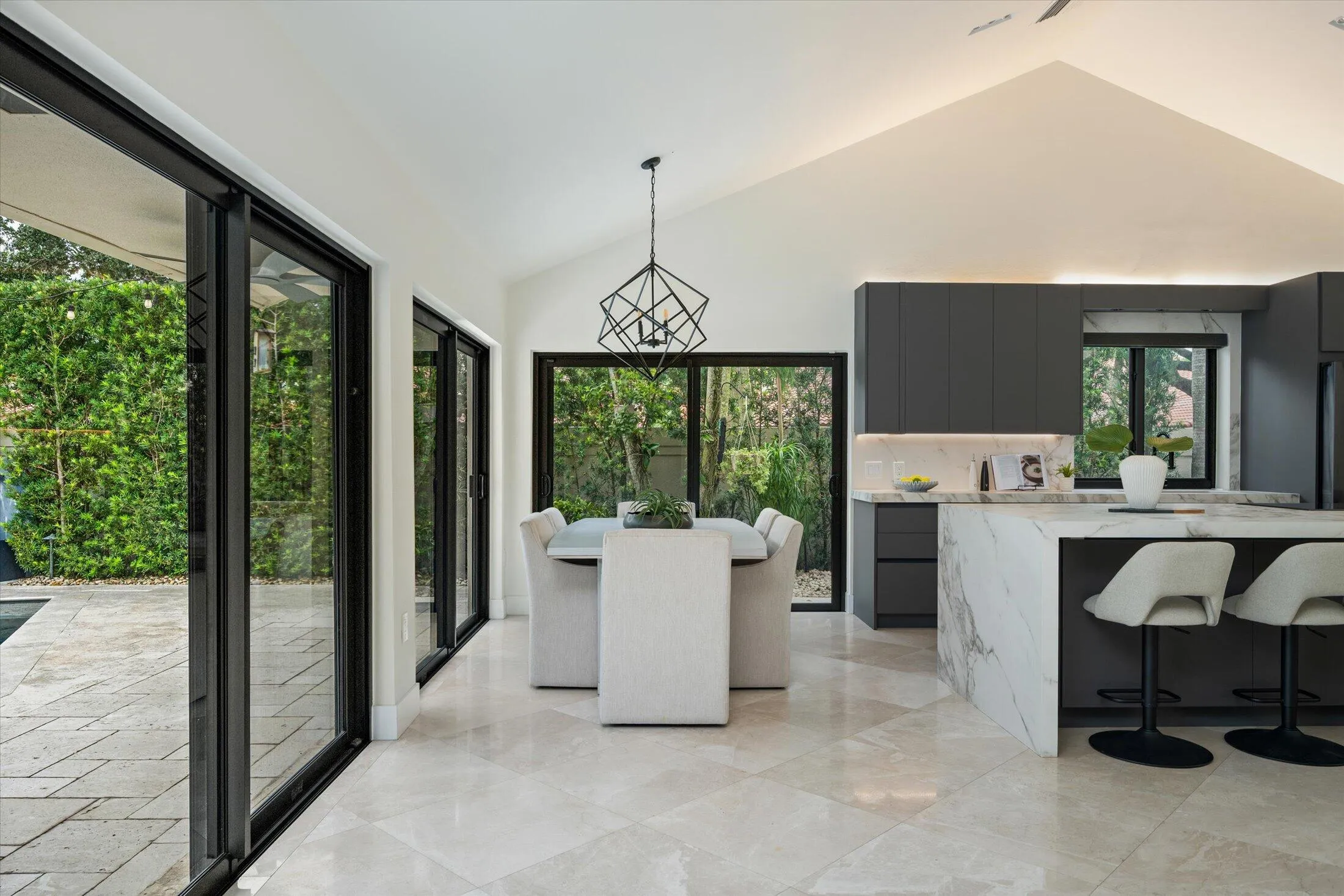 Vaulted ceiling with integrated lighting, expansive sliding glass doors, large format tile flooring, contemporary kitchen cabinetry, and a waterfall island with stone countertop