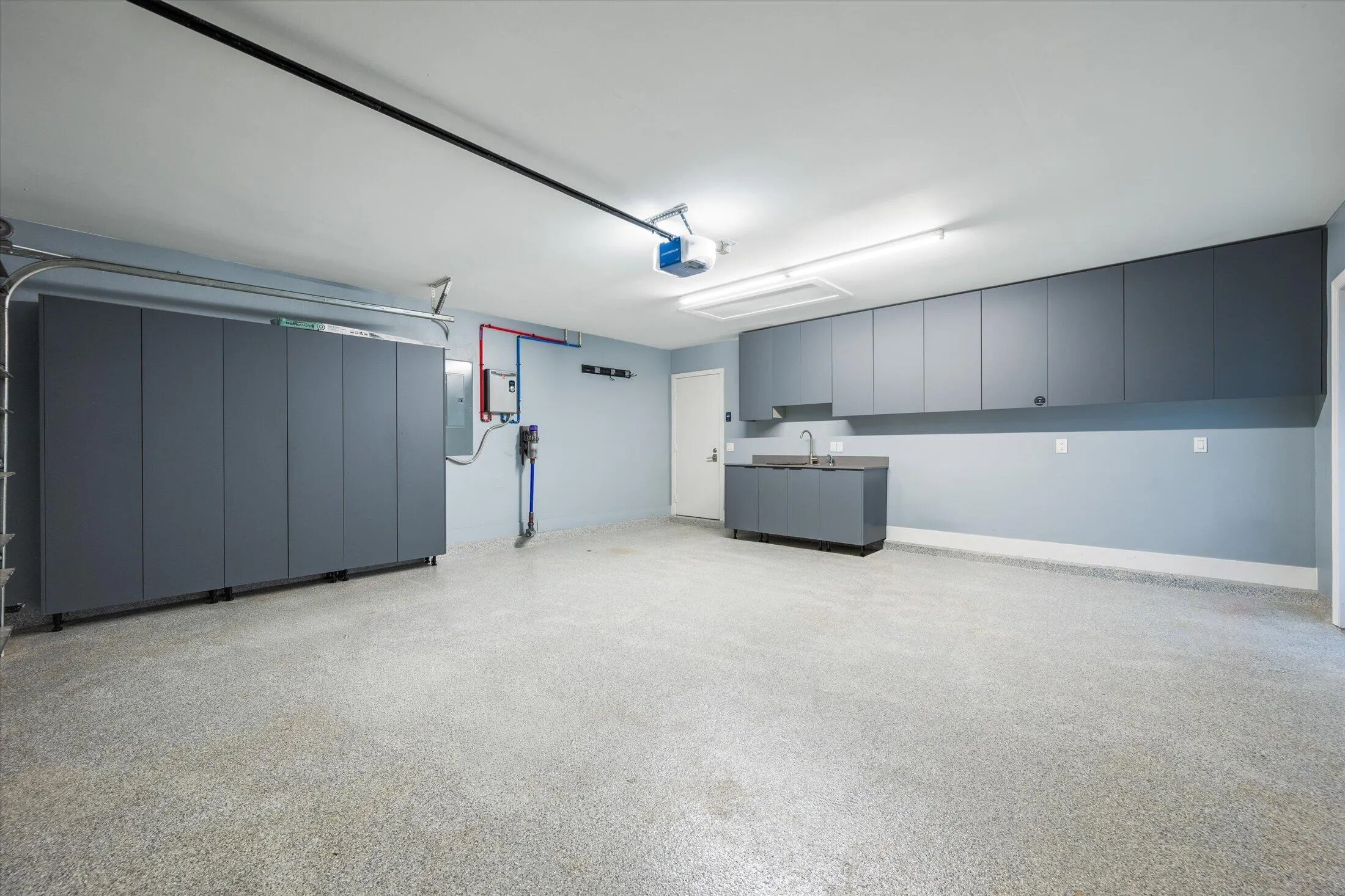Expansive garage featuring a speckled epoxy floor, extensive built-in storage cabinetry, a utility sink, and overhead fluorescent lighting