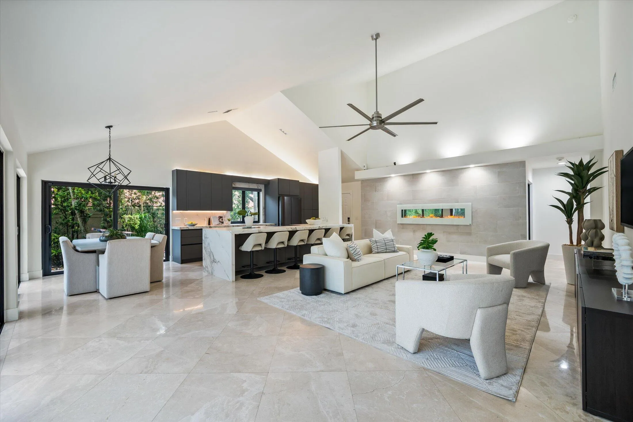 Vaulted ceilings, large format tile flooring, modern kitchen cabinetry, oversized kitchen island with waterfall countertop, and a wall-mounted linear fireplace