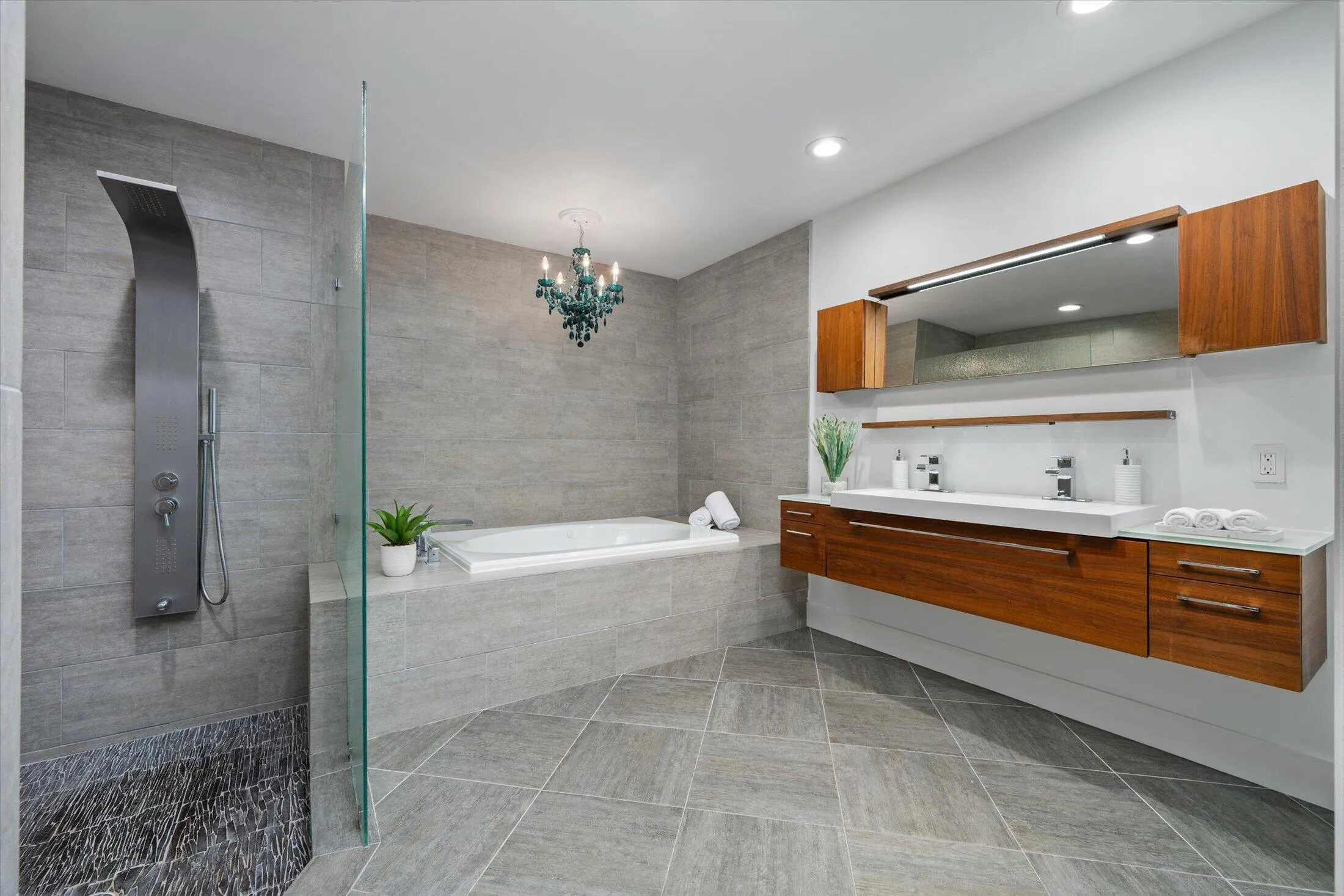 Integrated shower panel, large soaking tub, dual floating vanity with integrated sinks, wood-finish cabinetry, and recessed lighting