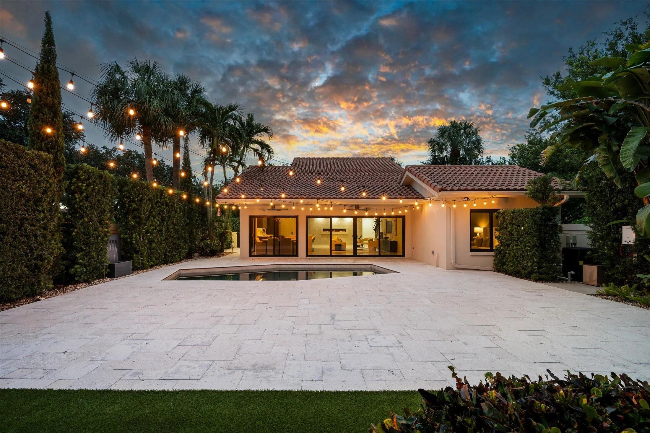 Pool area with extensive paver patio, lush perimeter landscaping, and a tile roof