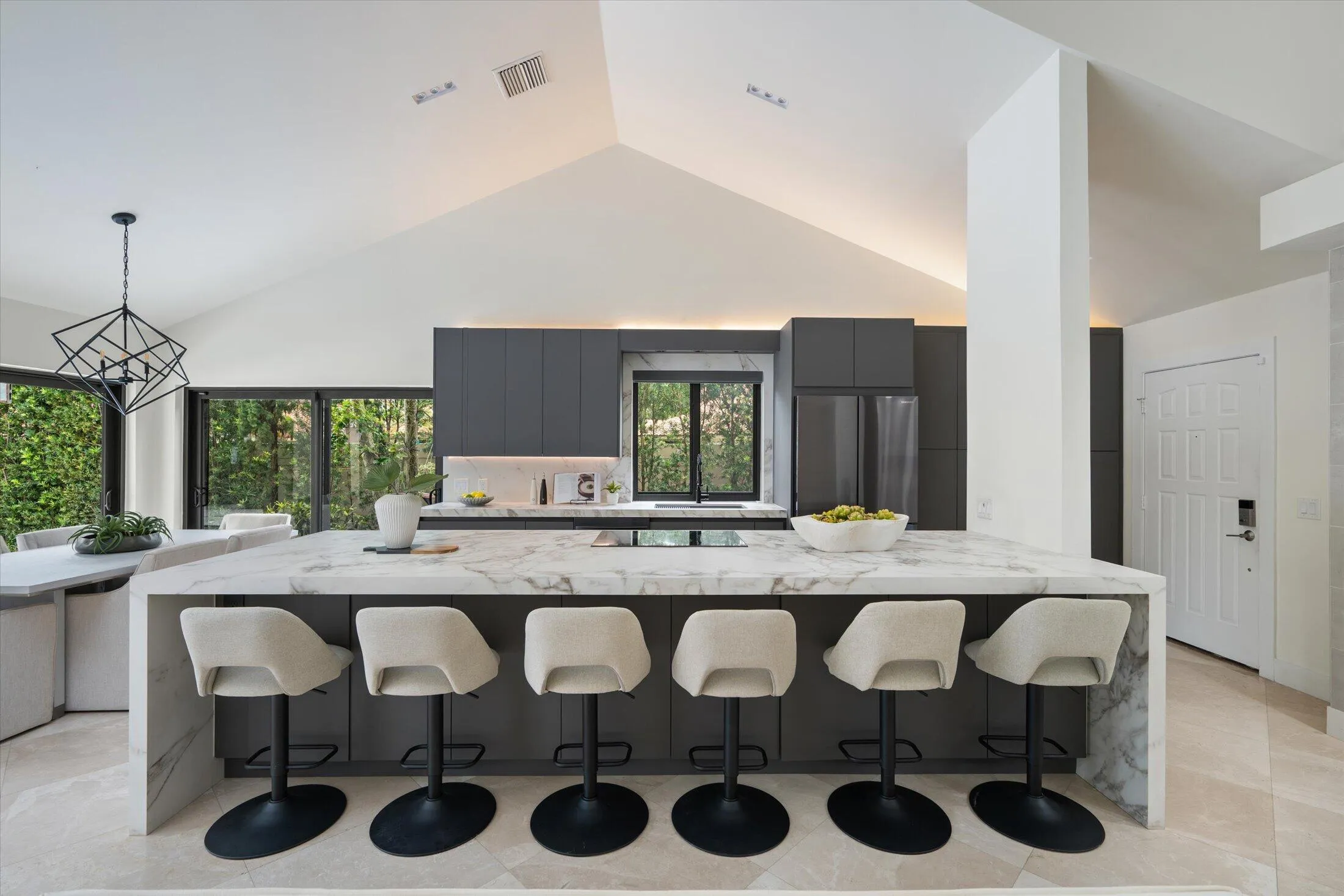 Vaulted ceiling with accent lighting, large kitchen island with waterfall edge, cabinetry, stainless steel appliances, and large windows