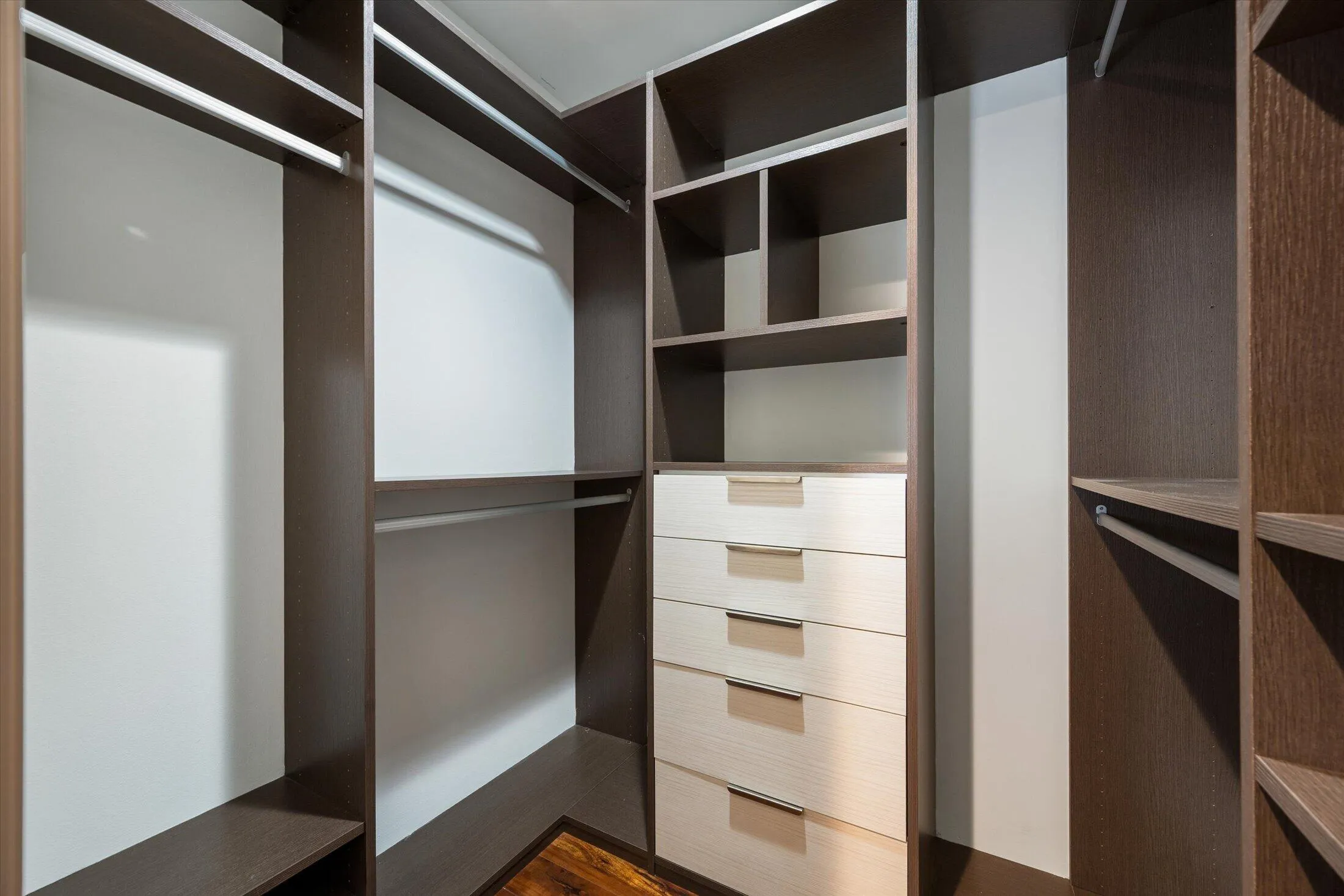 Custom closet system featuring dark wood-finish cabinetry, built-in shelving, multiple hanging rods, four light wood-finish drawers, and sleek drawer pulls