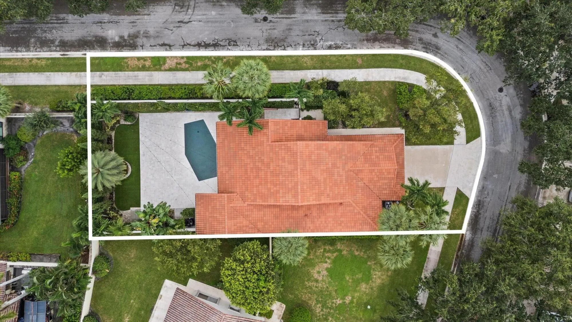Mediterranean-style roofline, geometric swimming pool, paved patio, mature landscaping, and an expansive driveway