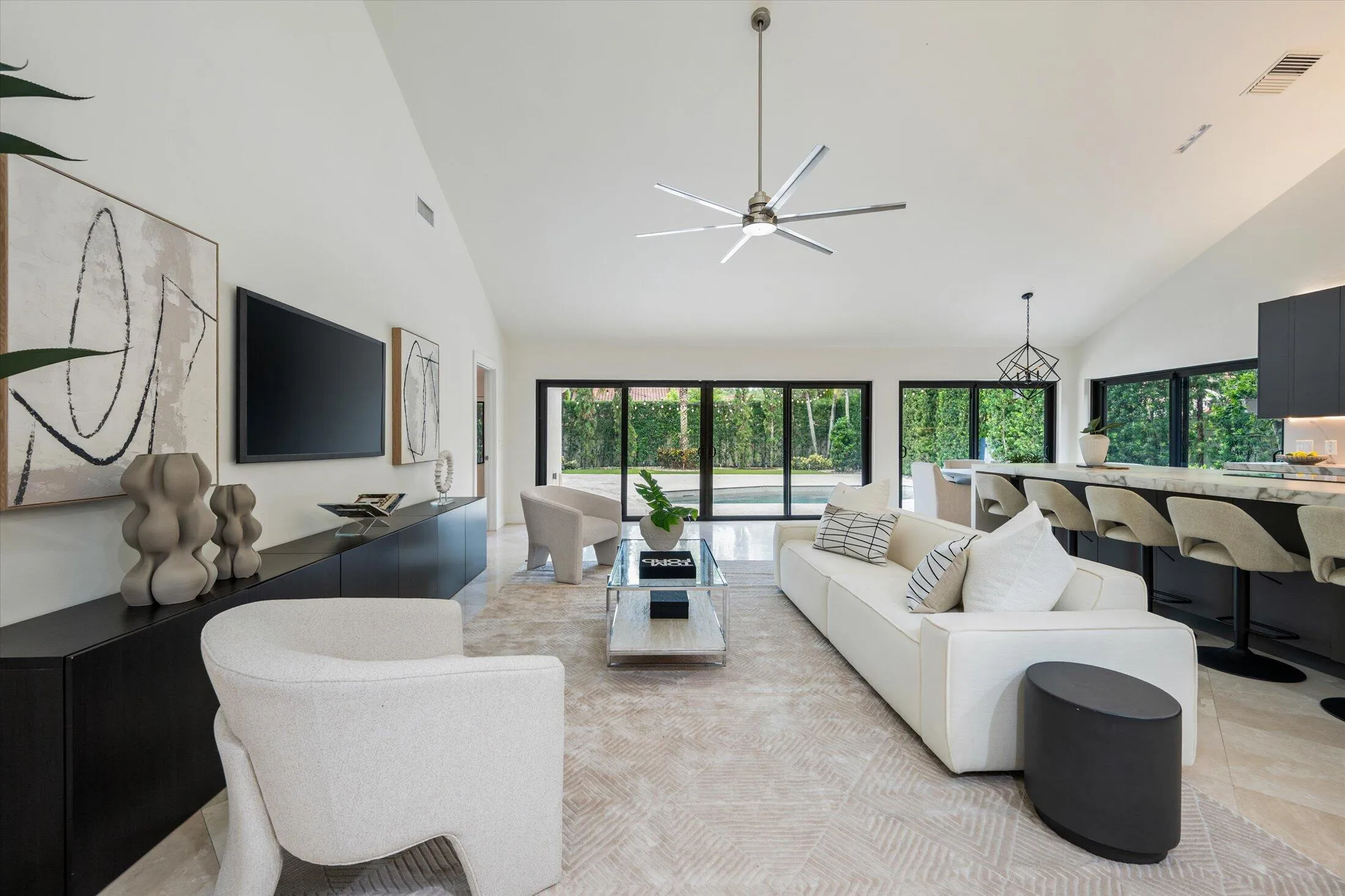 Vaulted ceilings, expansive glass doors, modern ceiling fan, built-in media console, and a kitchen island with seating
