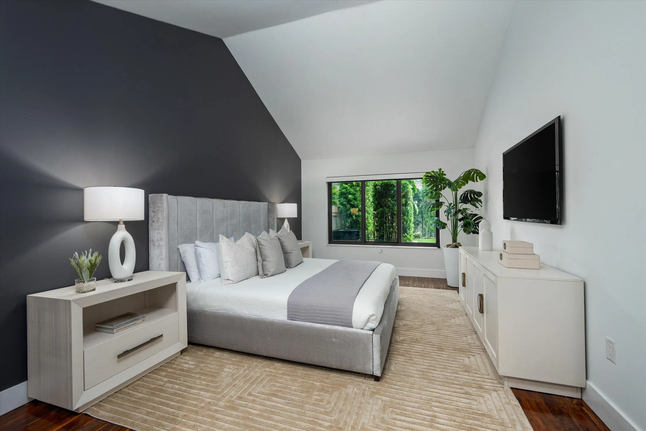 Vaulted ceilings, dark accent wall, wood-finish flooring, and a large window