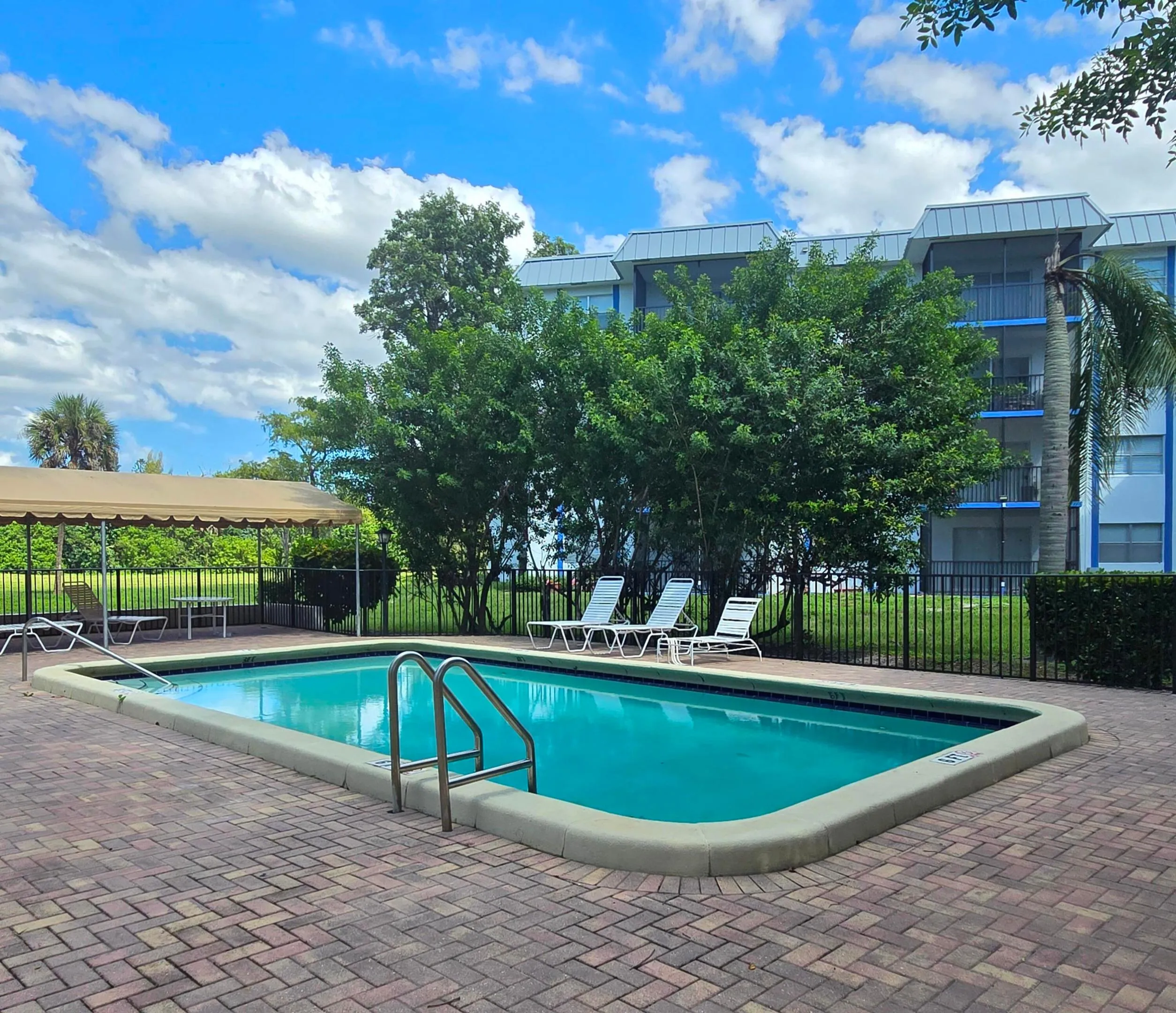 Community swimming pool surrounded by paver decking and a shaded outdoor seating area.