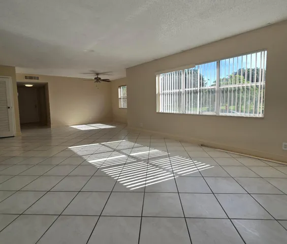 Spacious room with large windows, vertical blinds, ceiling fan and tiled flooring.