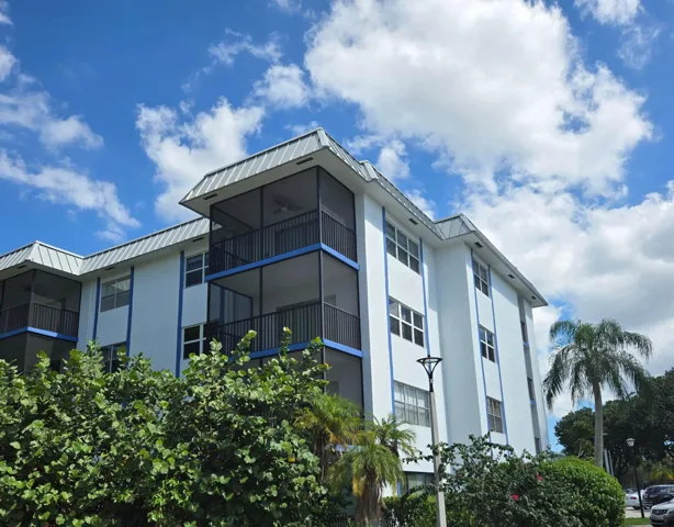 4 story building featuring screened balconies, newly painted white exterior and a metal roof mansard.