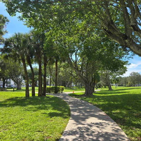 Lush landscaping featuring mature trees, palm trees, and a winding paved pathway.