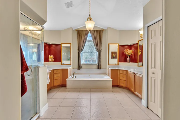 Spacious bathroom featuring a built-in soaking tub, a clear glass shower enclosure, dual vanity areas with wood cabinetry, and tiled flooring