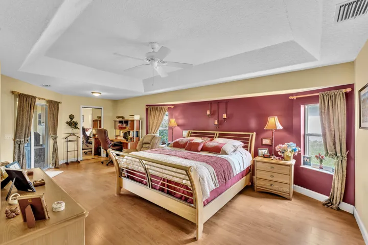 Tray ceiling with a ceiling fan, wood-finish flooring, and a glass-paneled door