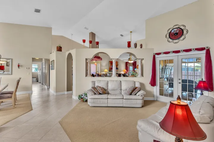 Vaulted ceilings with architectural archways, tile flooring, and double French doors to the exterior