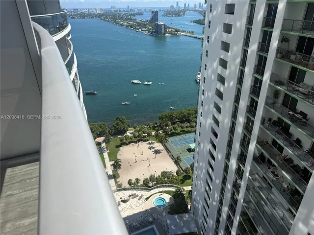 Expansive water body, multiple watercraft, sandy recreation area, tennis courts, and a circular pool feature