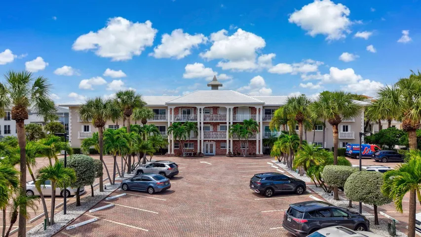 Multi-story residential building featuring a cupola, multiple balconies with white railings, and a red brick paver parking lot