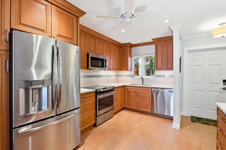 Kitchen featuring warm wood cabinetry, stainless steel appliances, a white tile backsplash, and light-toned flooring