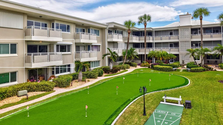Manicured putting green, shuffleboard court, multiple balconies, mature palm trees, and a central courtyard water feature