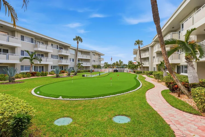Manicured grounds featuring a putting green, mature palm trees, and a winding brick pathway