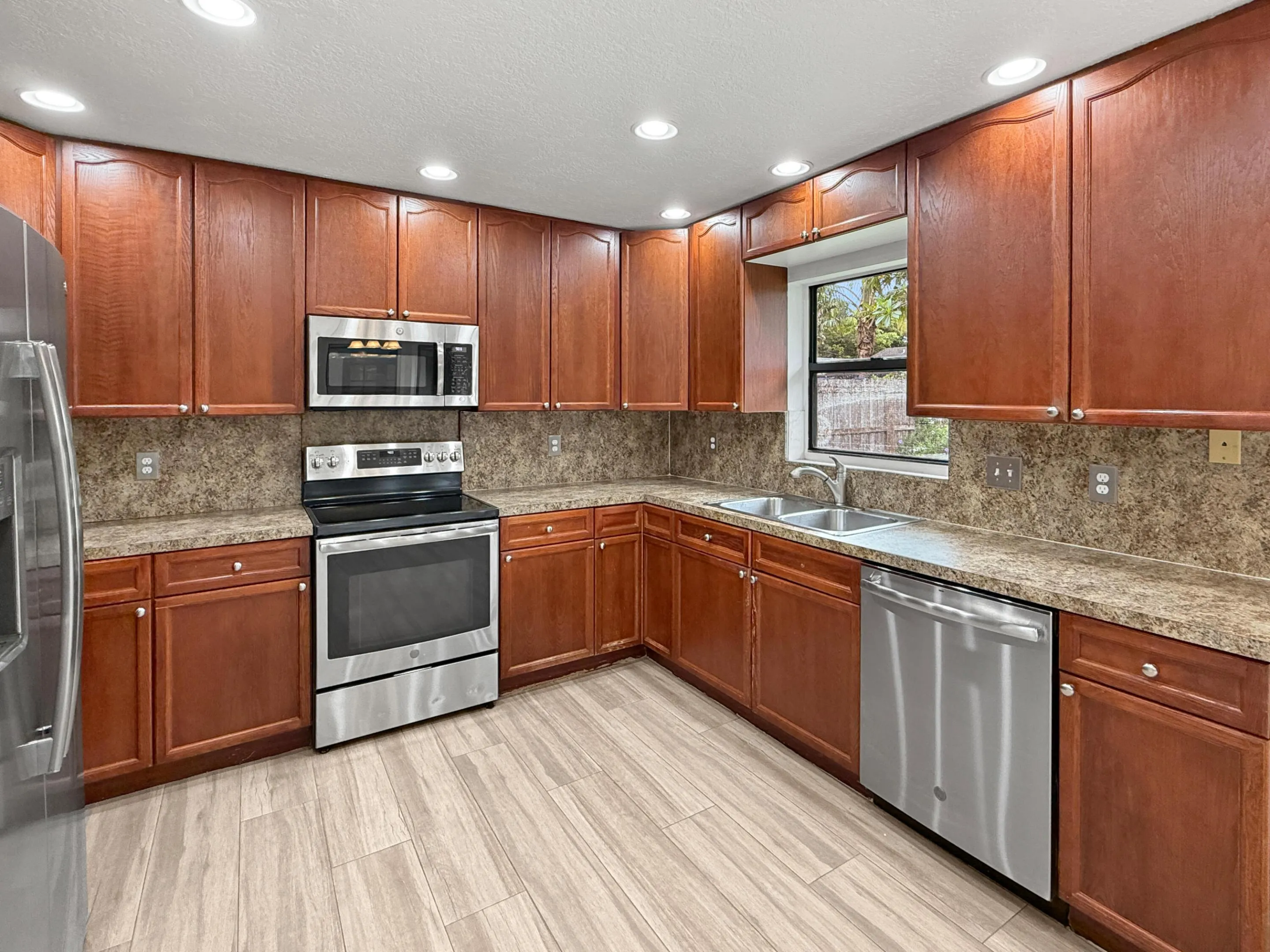 Kitchen featuring wood-finish cabinetry, stainless steel appliances, a double basin sink, recessed lighting, and wood-finish flooring
