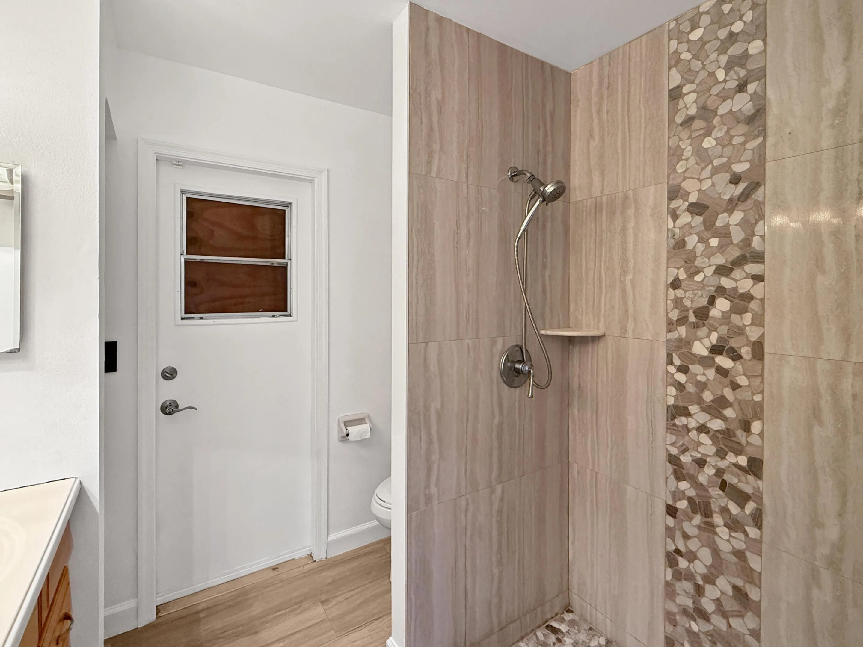 Walk-in shower featuring a tiled surround, decorative pebble tile accent, built-in shelf, and a handheld shower fixture