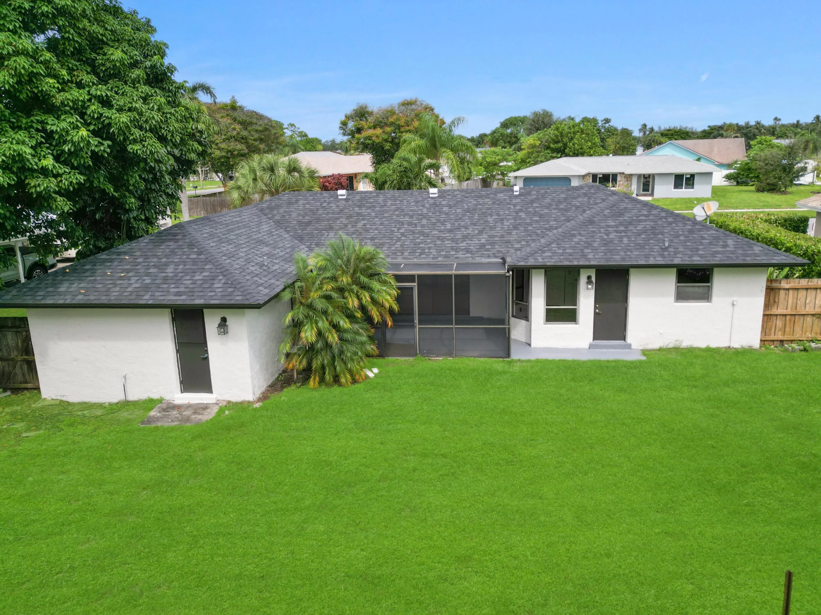 Expansive green lawn, dark shingle roof, screened patio, and exterior lighting fixtures