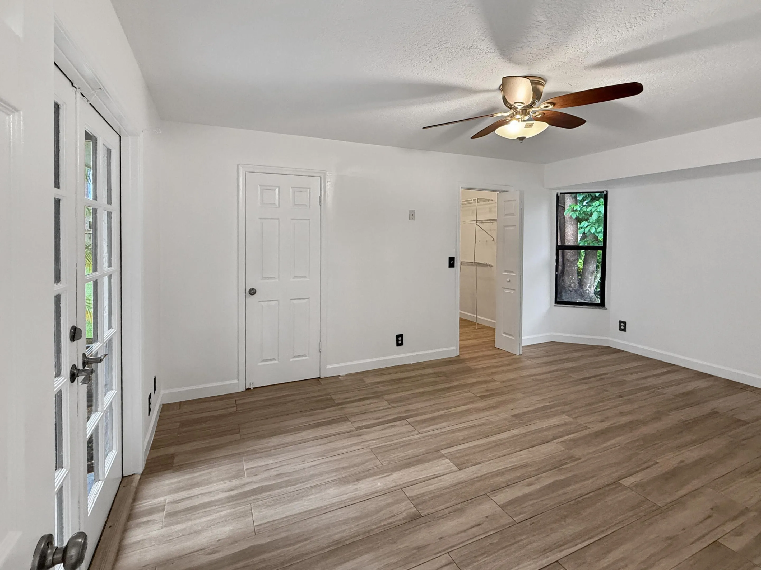 Wood-finish tile flooring, white walls, ceiling fan, French doors, and an additional doorway