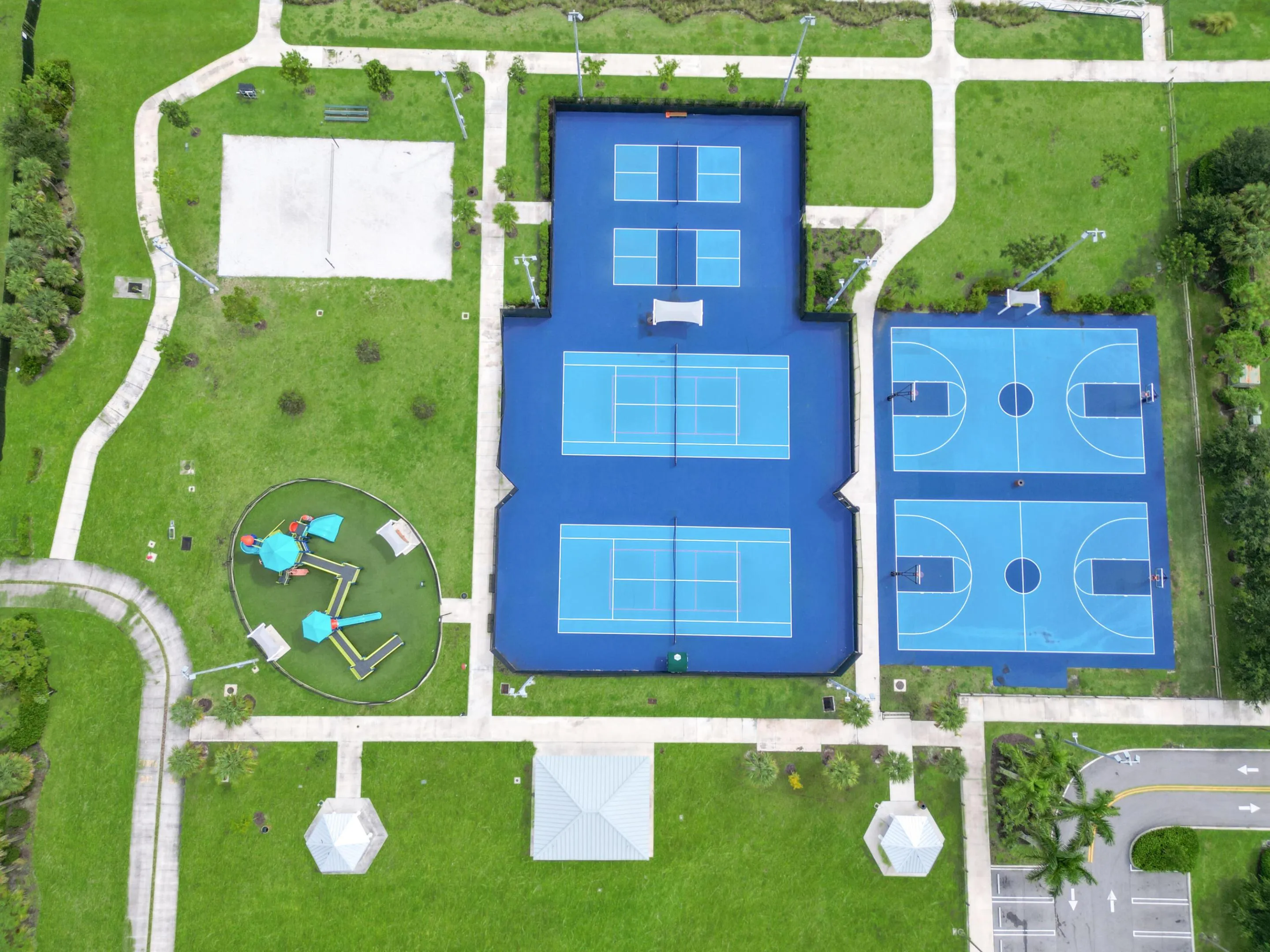 Outdoor recreational area featuring tennis courts, basketball courts, pickleball courts, a volleyball court, and a playground