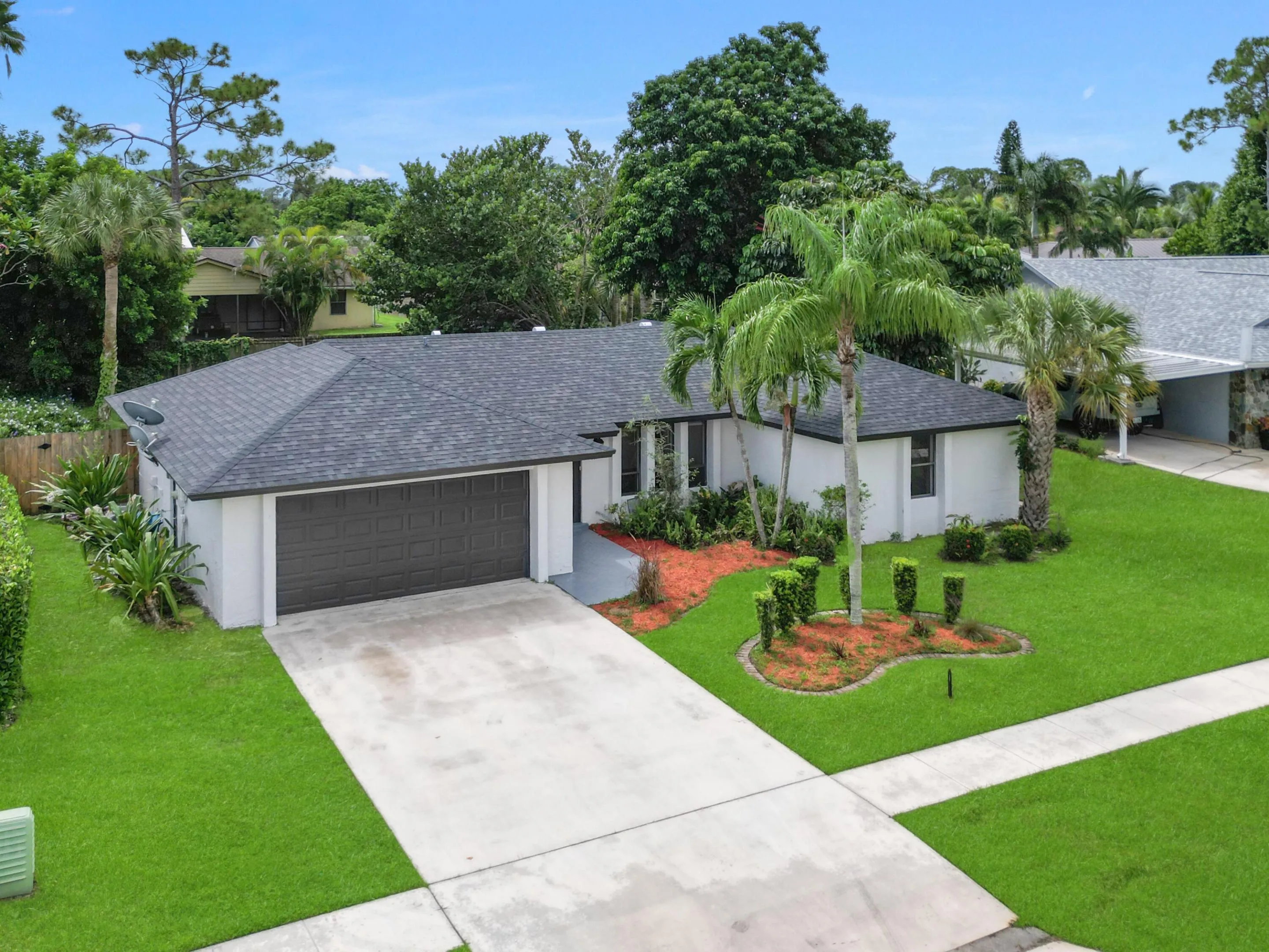 Asphalt shingle roof, attached two-car garage, concrete driveway, front yard landscaping, and mature palm trees