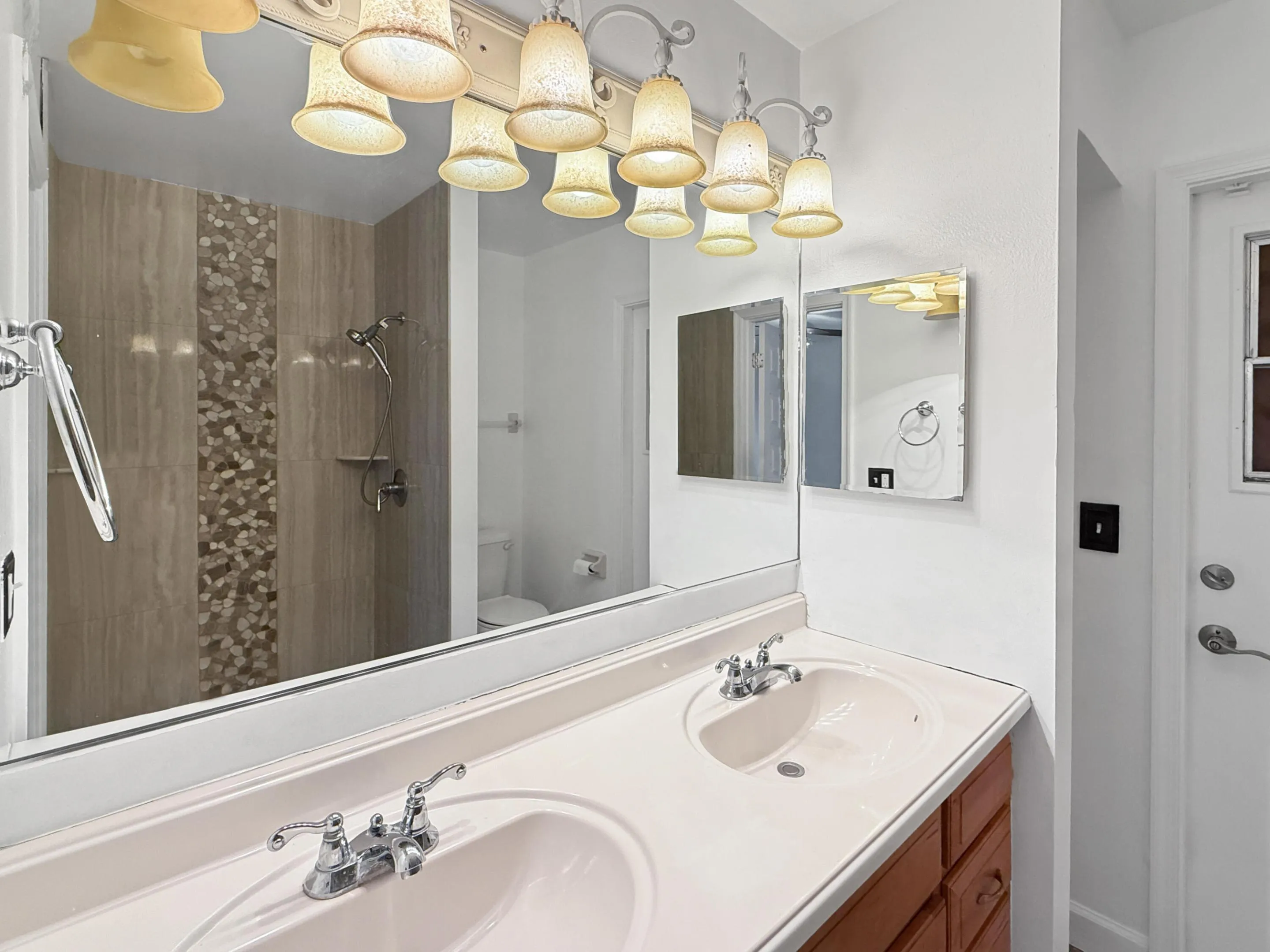 Double vanity with integrated sinks, wood-finish cabinetry, chrome fixtures, and overhead sconce lighting