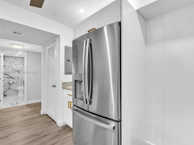 Stainless steel French door refrigerator, wood-finish flooring, white cabinetry with gold-tone hardware, stone countertop, and recessed lighting