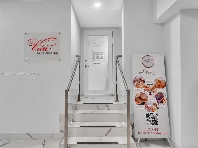 Entryway featuring stone-patterned tile stairs, a glass panel door, and brushed metal handrails with glass balustrades