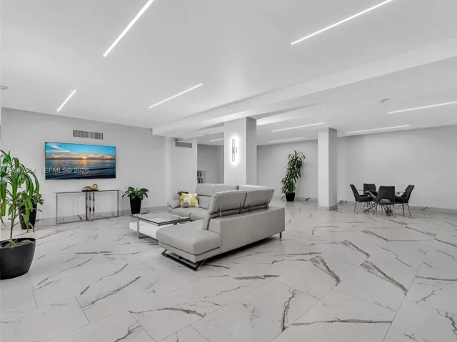 Open-concept interior featuring large-format tile flooring with a veined stone pattern, recessed linear lighting, and integrated vertical wall sconces