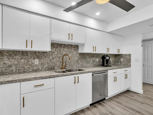 Kitchen featuring white slab-front cabinetry with metallic pulls, patterned stone-finish countertops and backsplash, integrated stainless steel dishwasher, and a high-arch bronze-tone faucet