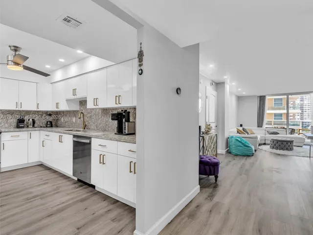 Kitchen featuring white cabinetry, stone-finish countertops, stainless steel dishwasher, and wood-finish flooring throughout