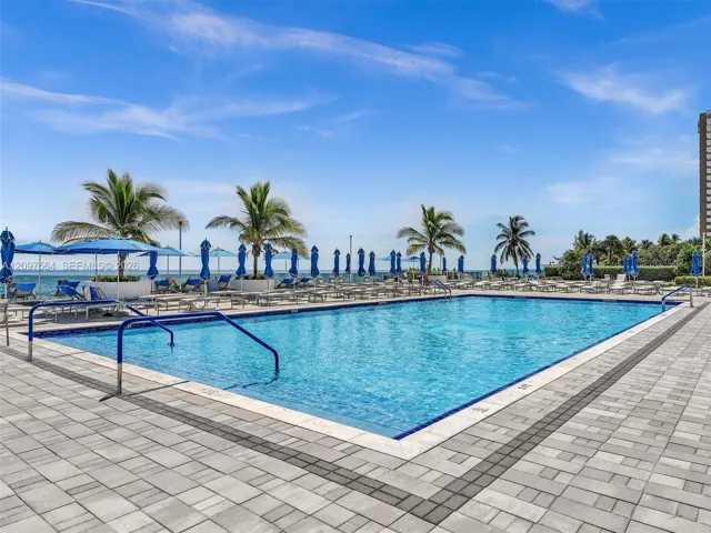 Rectangular swimming pool featuring a light-toned paver deck, perimeter border tile, and blue handrails
