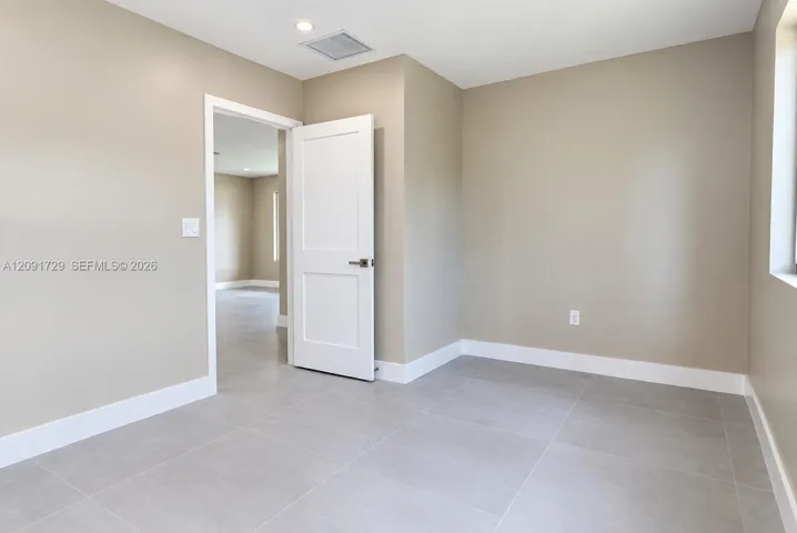 Neutral-toned interior featuring large-format ceramic tile flooring, a two-panel solid core door with satin nickel hardware, and recessed ceiling lighting