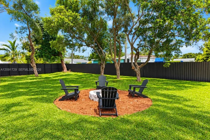 Private backyard featuring a stone-clad fire pit, mulch ground cover, mature trees, and a dark-toned perimeter fence