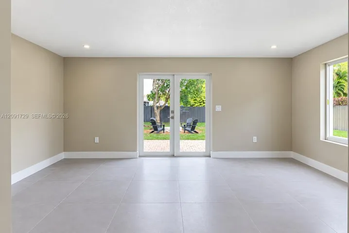 Neutral-toned interior featuring large-format tile flooring, recessed lighting, and dual glass French doors providing external access