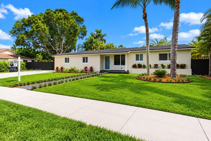 Single-story exterior featuring a light-toned stucco façade, dark roof shingles, an integrated concrete driveway, and professional landscaping with palm trees