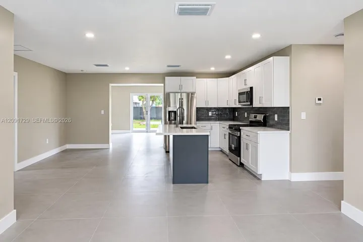 Kitchen featuring white shaker-style cabinetry, a contrasting dark-toned kitchen island, stainless steel appliances, dark tile backsplash, and large-format neutral tile flooring